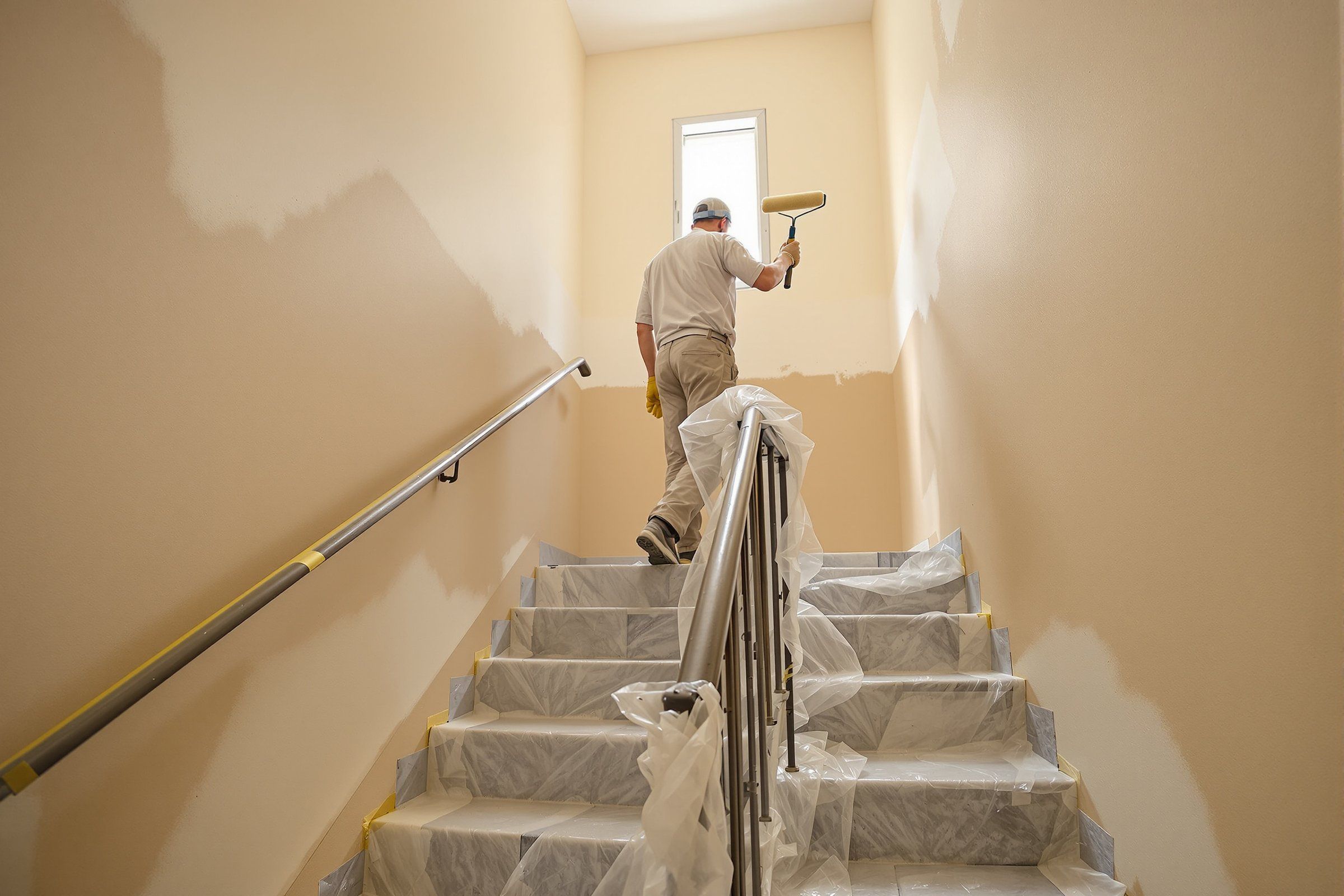 Pintor pintando la escalera de una comunidad con los peldaños protegidos con plástico